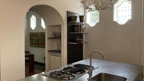 Cocina moderna con encimera de acero inoxidable, estufa a gas y pileta. Hay una lámpara de araña sobre la pileta y una ventana con vista al exterior.