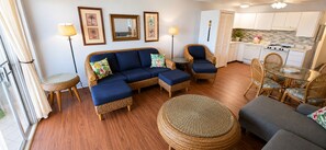 A living room with a sofa, chairs, a round table, and a kitchen in the background.