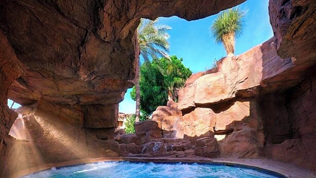 Un jacuzzi frente a un paisaje rocoso con palmeras y cielo despejado.