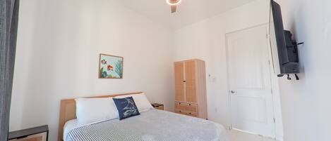 A bedroom with a bed, a wardrobe, a ceiling fan, a TV mounted on the wall, and a door.
