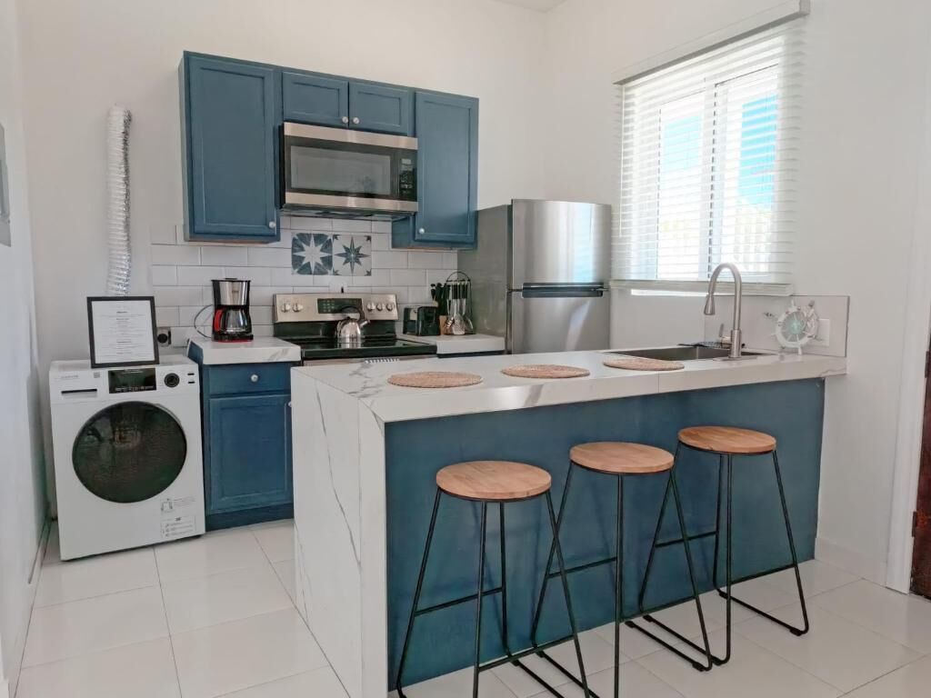 A compact kitchen with a central island, a washing machine, and a window with blinds.