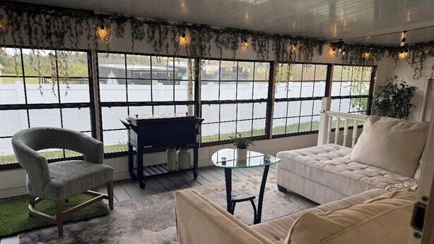 A cozy room with a sofa, armchair, and a small table, large windows with a view of the parking lot, and a ceiling with hanging plants. - PrivateOakForest RanchFirepit, BBQ&FamilyRetreat (Clermont)