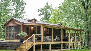 Une cabane en rondins dotée d’un porche couvert, de grandes fenêtres et d’un escalier menant à l’entrée.