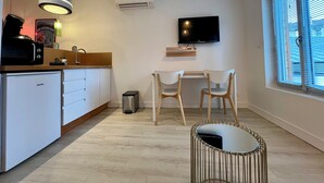 A modern kitchen with a built-in oven, a sink, and a coffee machine. There is a dining area with a table and two chairs. A TV is mounted on the wall above the table. - CASA BLUM #2 - Studio climatisé, à 2 pas de la gare (Brive-la-Gaillarde)