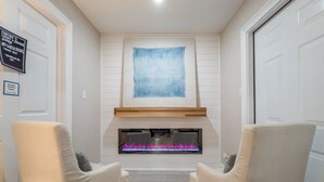 A room with two beige armchairs facing a fireplace with a blue abstract painting above it. - Beach Access, Hot Tub, Ping Pong Table, Bikes! (Tybee Island)