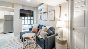 A modern living room with a grey sofa, a round coffee table, and a TV mounted on the wall. - Beach Access, Hot Tub, Ping Pong Table, Bikes! (Tybee Island)