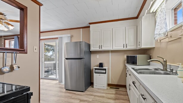 A modern kitchen with white cabinets, a stainless steel refrigerator, a microwave, and a sink. - Coastal Beaufort Getaway Near Downtown & Beaches (Beaufort)