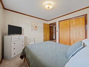 Una camera da letto con un letto, una cassettiera, una televisione e una porta che dà su un'altra stanza.
