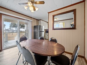 A dining area with a wooden table and chairs, a ceiling fan, and a kitchen in the background.
