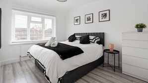Ein modernes Schlafzimmer mit einem großen Bett, einem Nachttisch, einem Heizkörper und einem Fenster mit Jalousien.