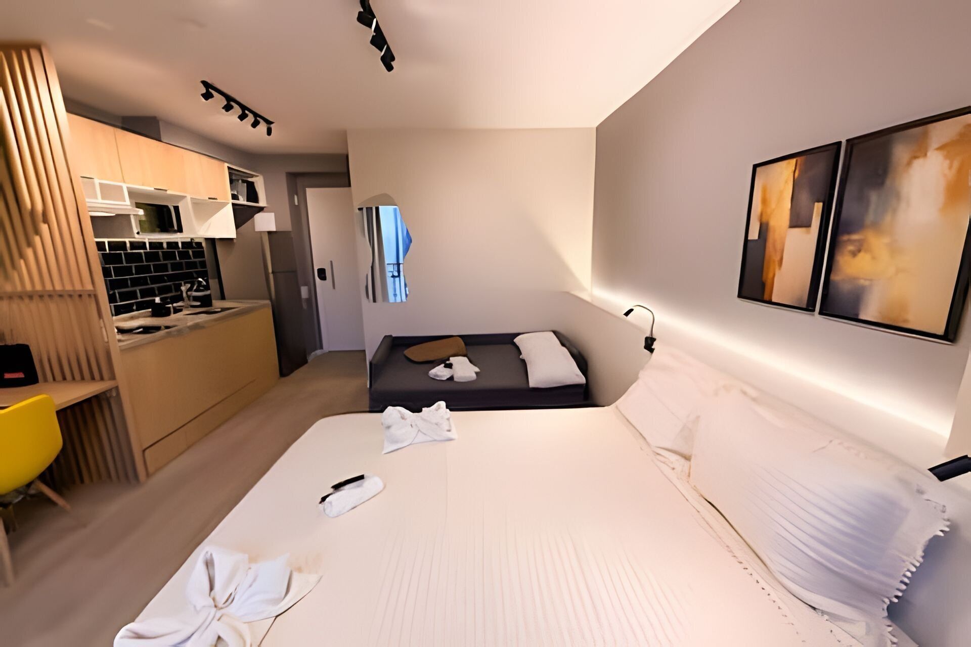 A hotel room with a bed, a desk, a kitchenette, and a bathroom.