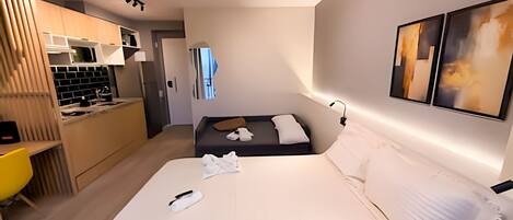 A hotel room with a bed, a desk, a kitchenette, and a bathroom.