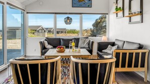 A modern living room with a sofa, two armchairs, a coffee table, and a large window offering a view of houses and greenery. - "Månviva" - 250m from the sea by Interhome (Løkken)