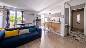 A modern living room with a blue sofa, a dining table, and a kitchen area with a bar. - L'Écrin Toulousain - Piscine partagée et parking (Toulouse)