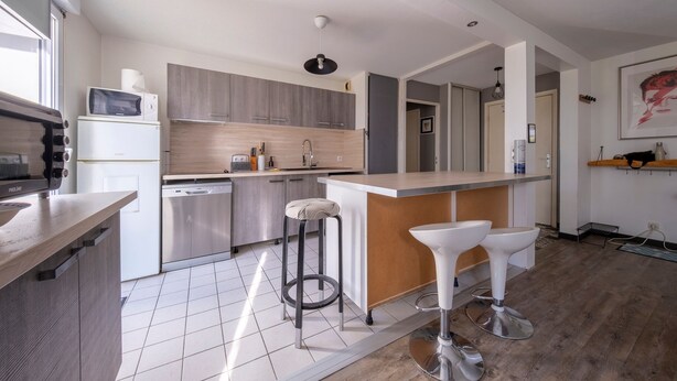 A modern kitchen with a central island, bar stools, and a microwave. - L'Écrin Toulousain - Piscine partagée et parking (Toulouse)