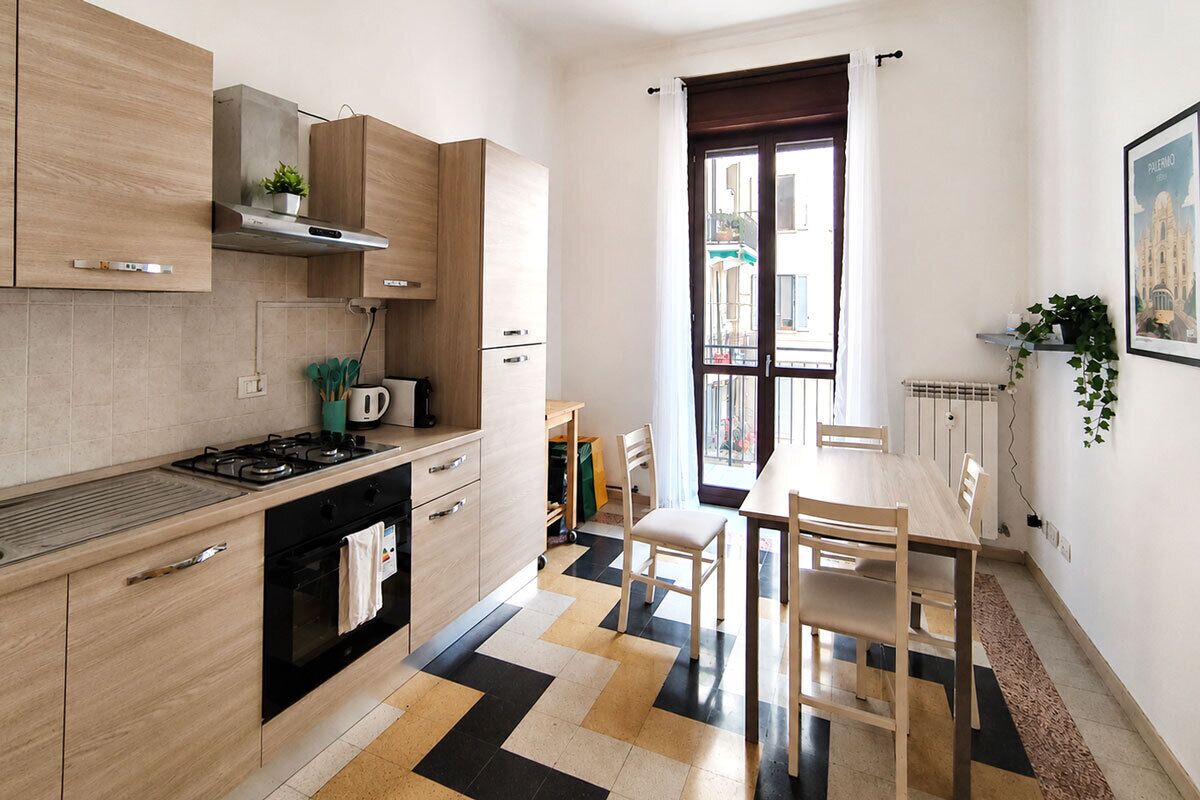 A modern kitchen with a gas stove, oven, and wooden cabinets. There is a dining area with a table and chairs.