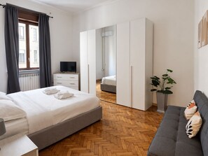A modern hotel room with a bed, a sofa, a TV, a wardrobe, and a potted plant. - BIG Smart Goldoni [Duomo-M4 Lin Airport] (Milan)