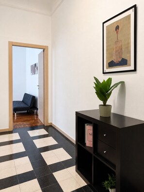 A hallway with a checkered floor, a black sofa, a framed artwork, and a potted plant on a black console table. - BIG Smart Goldoni [Duomo-M4 Lin Airport] (Milan)
