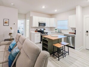 A modern kitchen with white cabinets, a microwave, a stove, and a sink. There is a wooden island with stools, and a dining table with chairs. - Salty Joe's-WindMark Beach-Pools-Golf Cart-Sleeps 10-InLaw Suite (Port St. Joe)