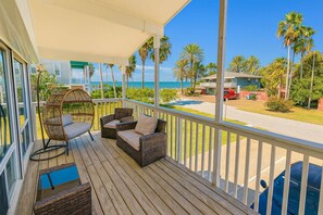 A wooden deck with wicker furniture, a hanging chair, and a view of the beach and palm trees. - Unique 2 in 1  * BayViews * Pool (South Padre Island)