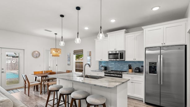 A modern kitchen with white cabinets, a stainless steel refrigerator, and a central island with stools. - Beach House - Sunny Sands  (Panama City Beach)
