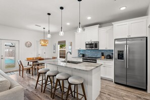 A modern kitchen with white cabinets, a stainless steel refrigerator, and a central island with stools. - Beach House - Sunny Sands  (Panama City Beach)