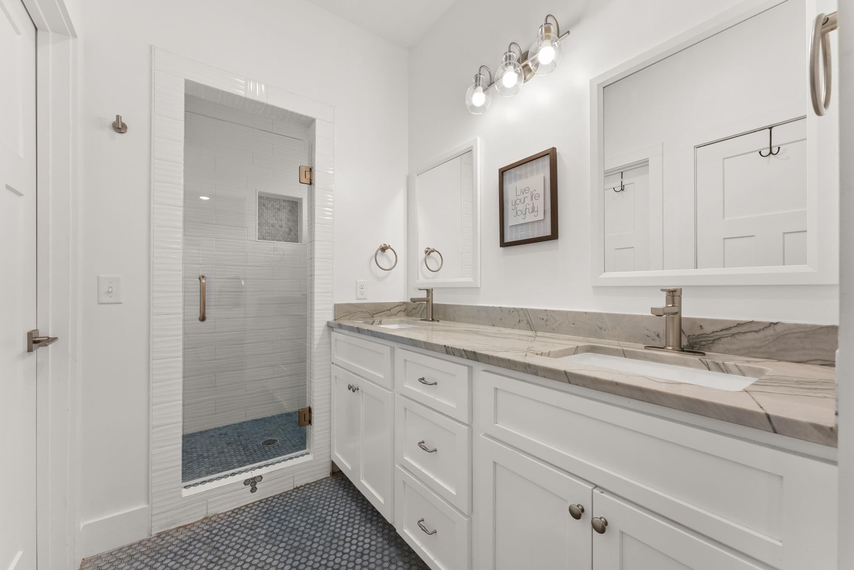 A modern bathroom with a glass-enclosed shower, white cabinetry, and a marble countertop.