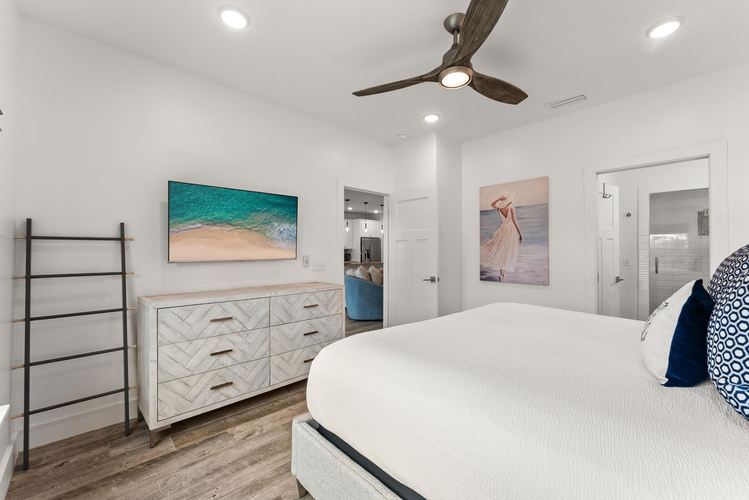 Un dormitorio con cama, cómoda, ventilador de techo y obras de arte en las paredes.
