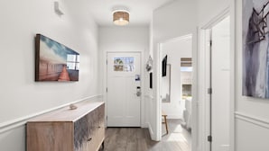 A hallway with a wooden console table, a painting, and a door leading to a room. - Beach House - Sunny Sands  (Panama City Beach)