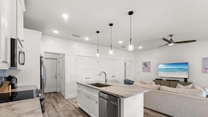 A modern kitchen with a built-in dishwasher, a dining area with a sofa, and a ceiling fan. - Beach House - Sunny Sands  (Panama City Beach)