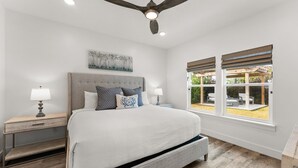 A bedroom with a large bed, two bedside tables, a ceiling fan, and a window with blinds. - Beach House - Sunny Sands  (Panama City Beach)