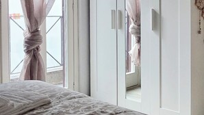 Un dormitorio con cama, armario y ventana con cortinas.
