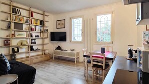 Una sala de estar acogedora con una estantería, un televisor de pantalla plana, una mesa de comedor con sillas y un ventanal con vistas a zonas verdes.