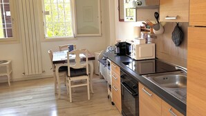 Una cocina compacta con encimera de madera, horno integrado y lavamanos. Hay una mesa de comedor con sillas y una ventana con vistas a zonas verdes.