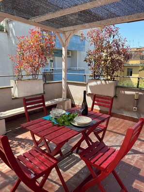 A red wooden table set with plates, glasses, and a bottle, surrounded by red chairs on a tiled patio with potted plants. - Terracehome71 - Terrace Apartment Near the Vatican Museums and the Cipro Metro (Line A) Station (Roma)