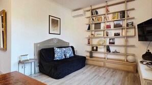 Una habitación con un sofá negro, una estantería de madera, un televisor de pantalla plana y una pequeña mesa.