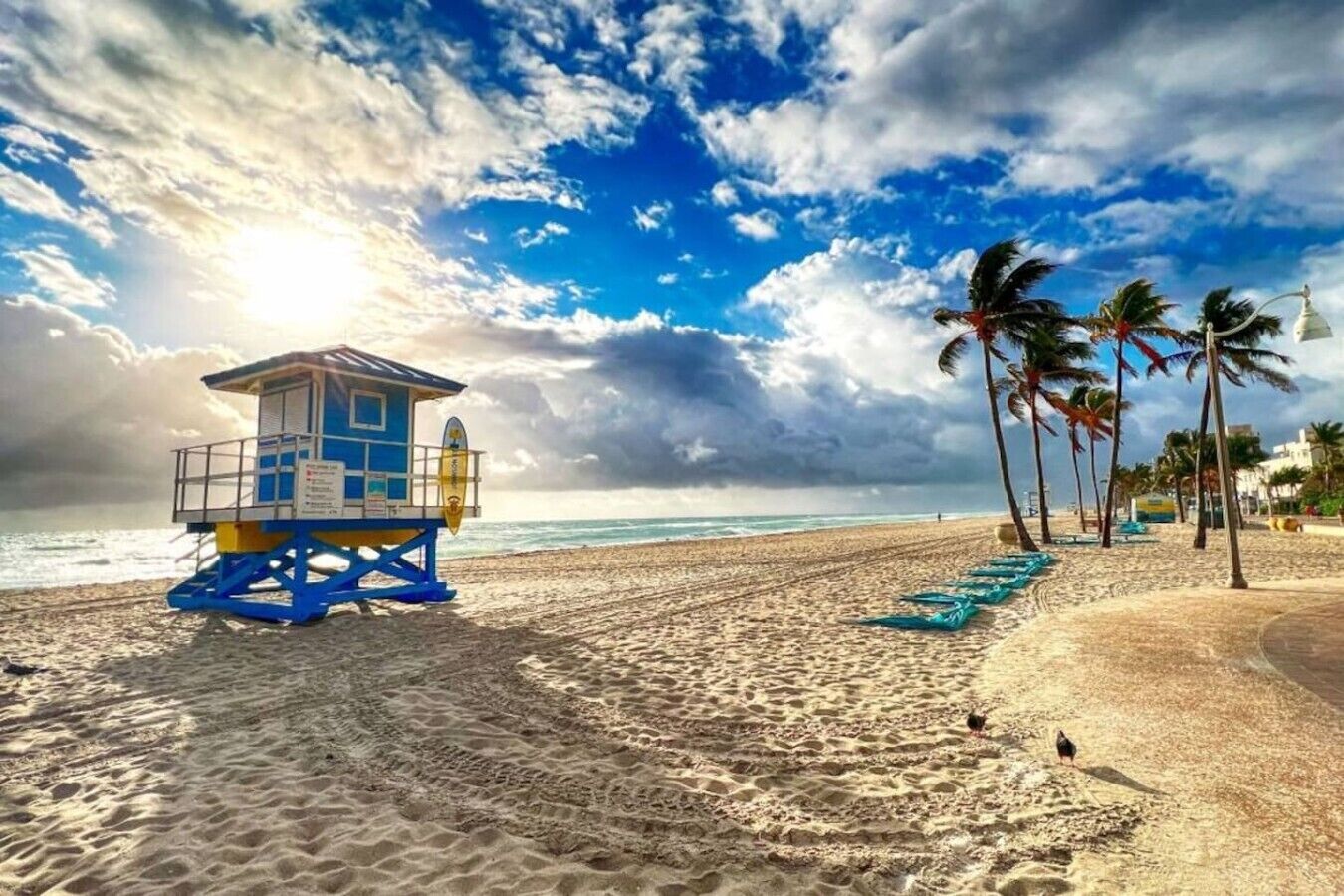 A lifeguard tower on a sandy beach with palm trees and a clear sky.