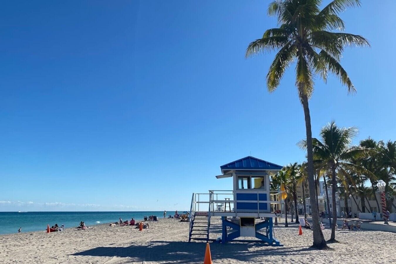 Una playa con una torre de salvavidas, palmeras y un cielo azul despejado.