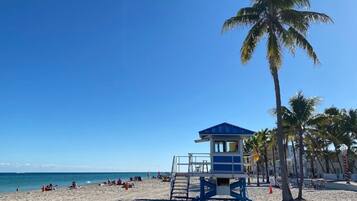Una playa con una torre de salvavidas, palmeras y un cielo azul despejado.
