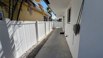 A narrow concrete pathway flanked by white fences, leading to a building with a flat roof and a small window.