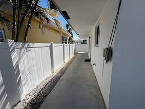 A narrow concrete pathway flanked by white fences, leading to a building with a flat roof and a small window. - Beach Escape 2BR • 5 min FLL • Free Parking (Dania Beach)