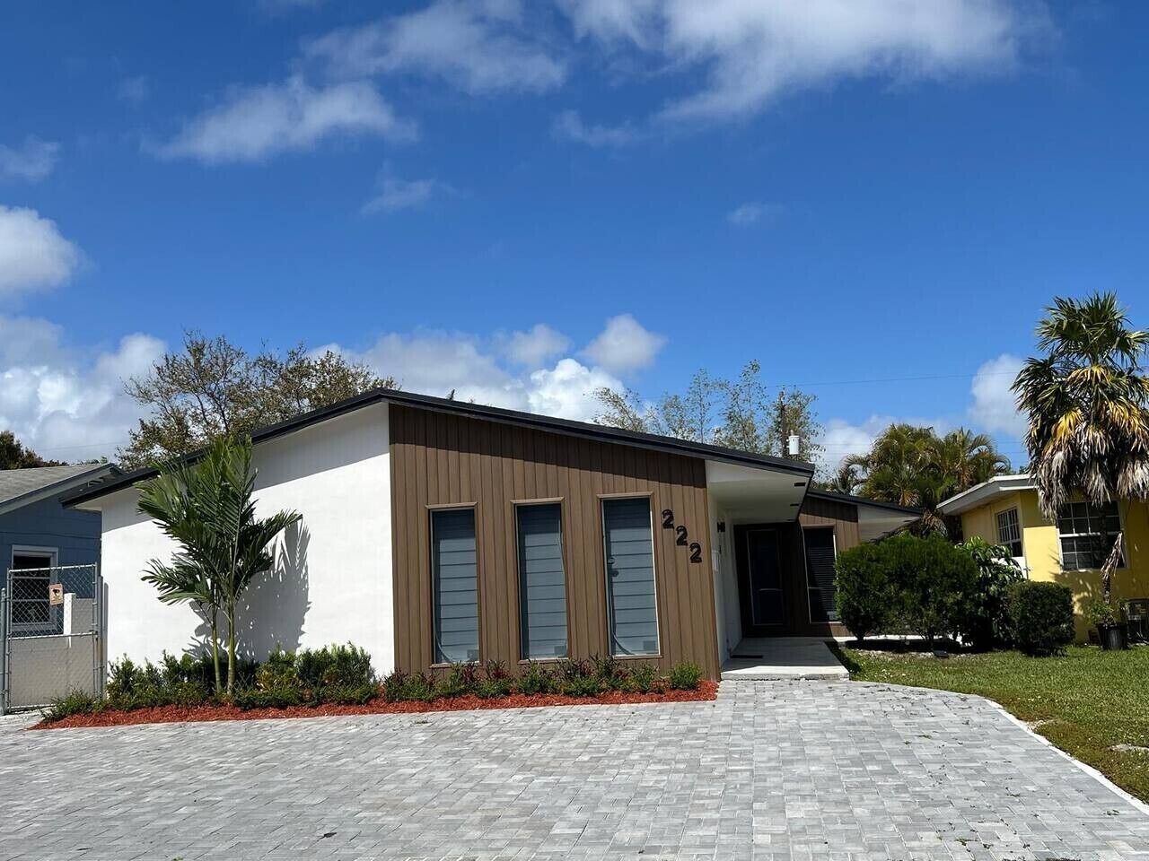 A modern two-story house with a paved driveway, a small garden, and a clear blue sky.
