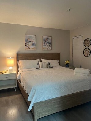 A neatly made bed with a wooden headboard, a bedside lamp, and two wall-mounted paintings of birds. - Beach Escape 2BR • 5 min FLL • Free Parking (Dania Beach)