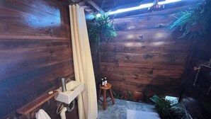 A bathroom with wooden walls, a sink, a shower curtain, a small stool, and a mat on the floor. - Lavender Dream in Glamping Rincón de Lavanda (Texcoco de Mora)