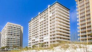 A beachfront hotel with multiple floors, balconies, and a sandy beach in the foreground. - Bluewater 103 | Beach Front (Orange Beach)