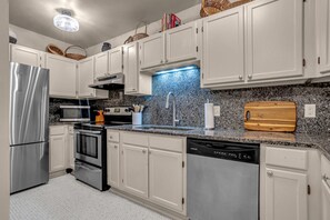 Eine moderne Küche mit weißen Schränken, Edelstahlgeräten, einer Granitarbeitsplatte und einem Holzschnittbrett.