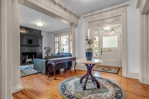 A spacious living room with a fireplace, a blue sofa, a round table with a vase, and a patterned rug. - 1896 Victorian Mansion - Steps from Forsyth (Savannah)