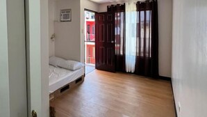 Une pièce comprenant un lit, un ventilateur de plafond, une fenêtre avec des rideaux et une porte donnant sur une autre pièce.