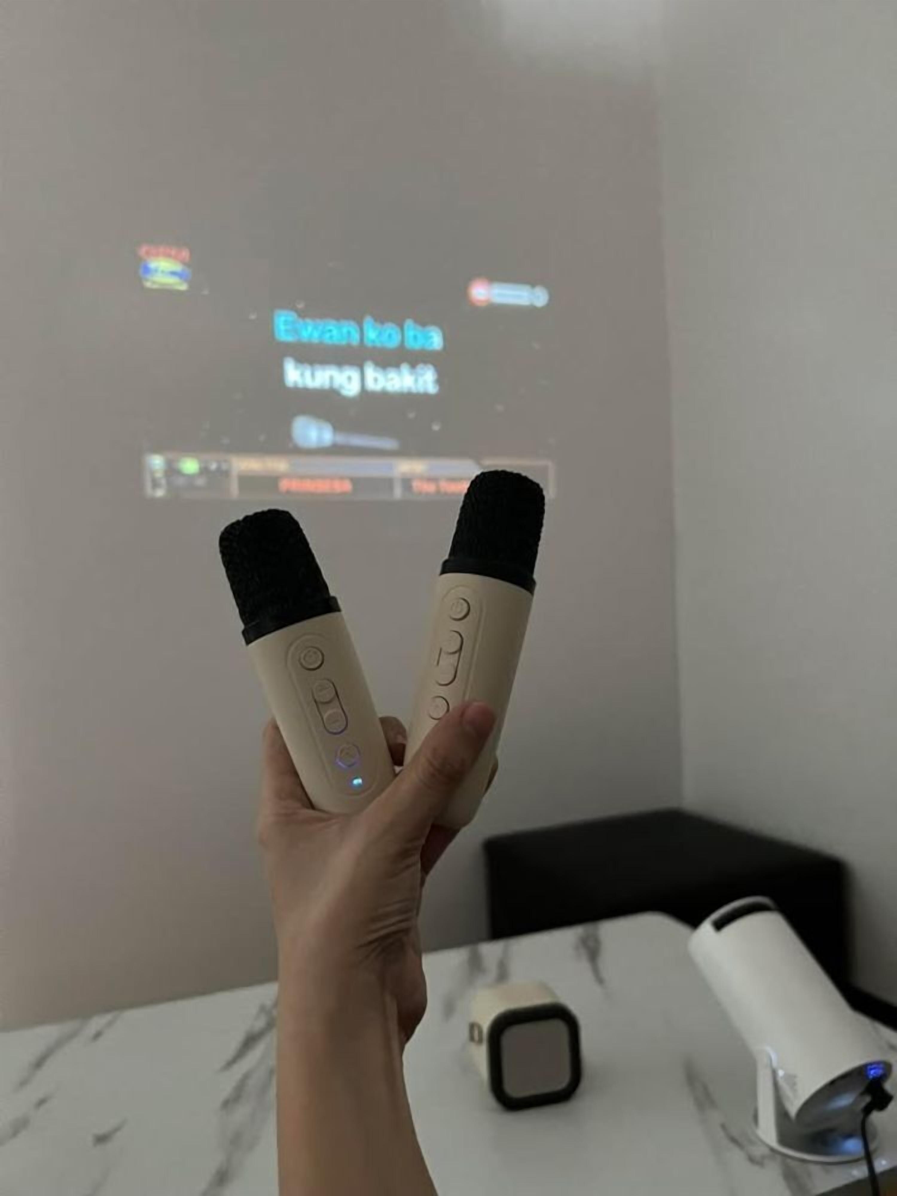 Mão segurando dois controles remotos em frente a uma tela de projeção exibindo texto.