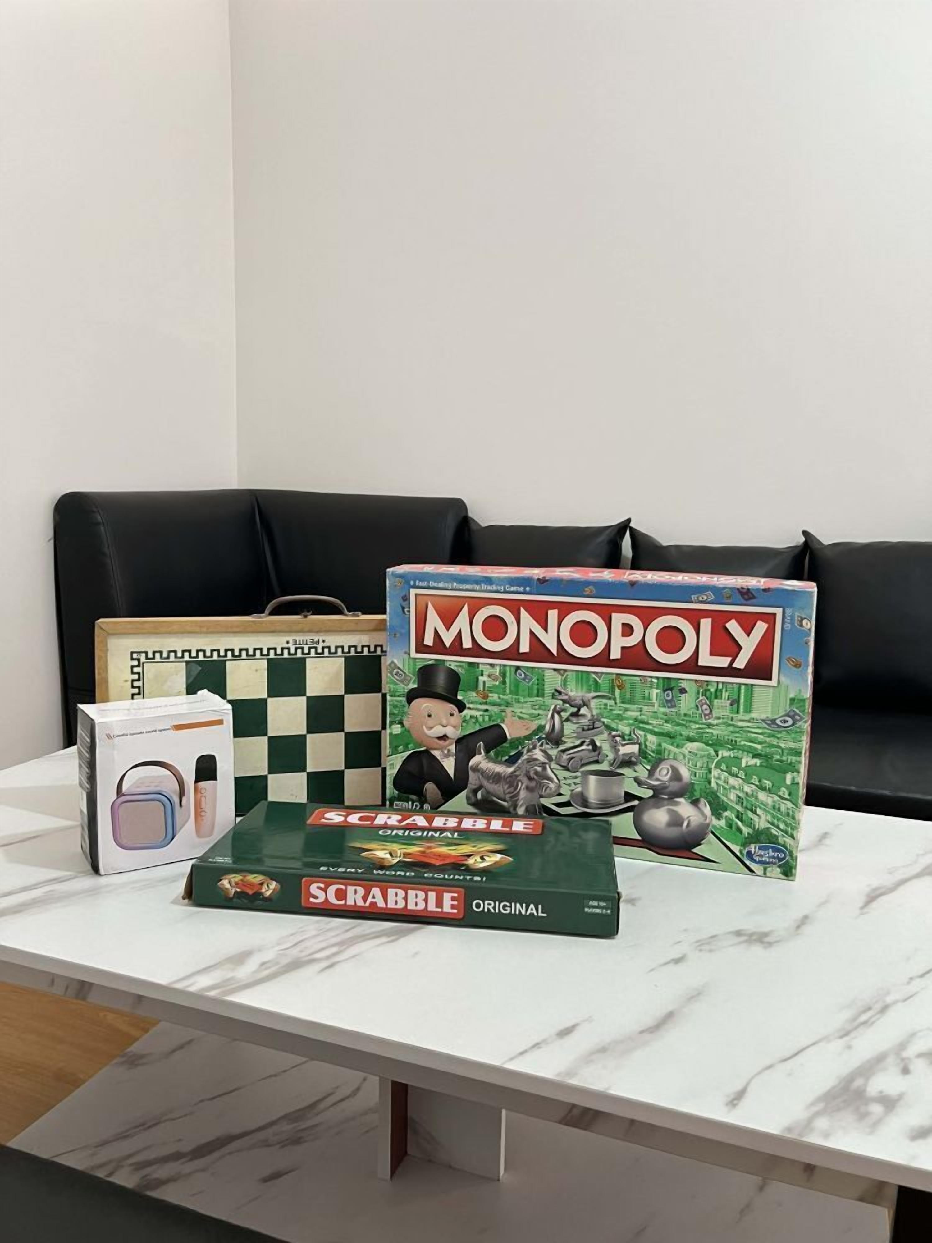 A table with Monopoly and Scrabble games, a framed chessboard, and a Scrabble tile bag.